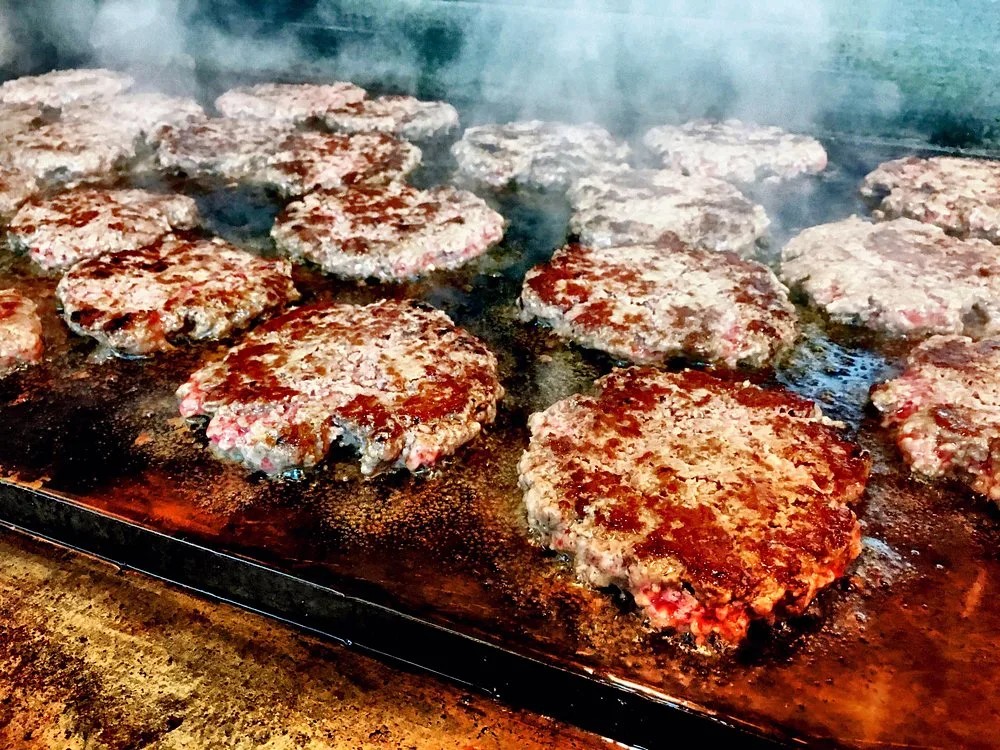 Hand-pattied burger patties grilling on the flat top, fresh ground chuck