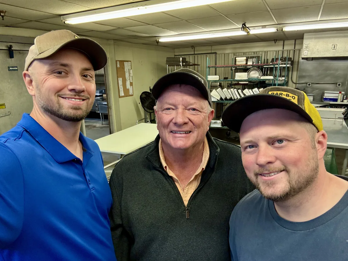 Three BBQ King employees smiling for a selfie together in the prep kitchen
